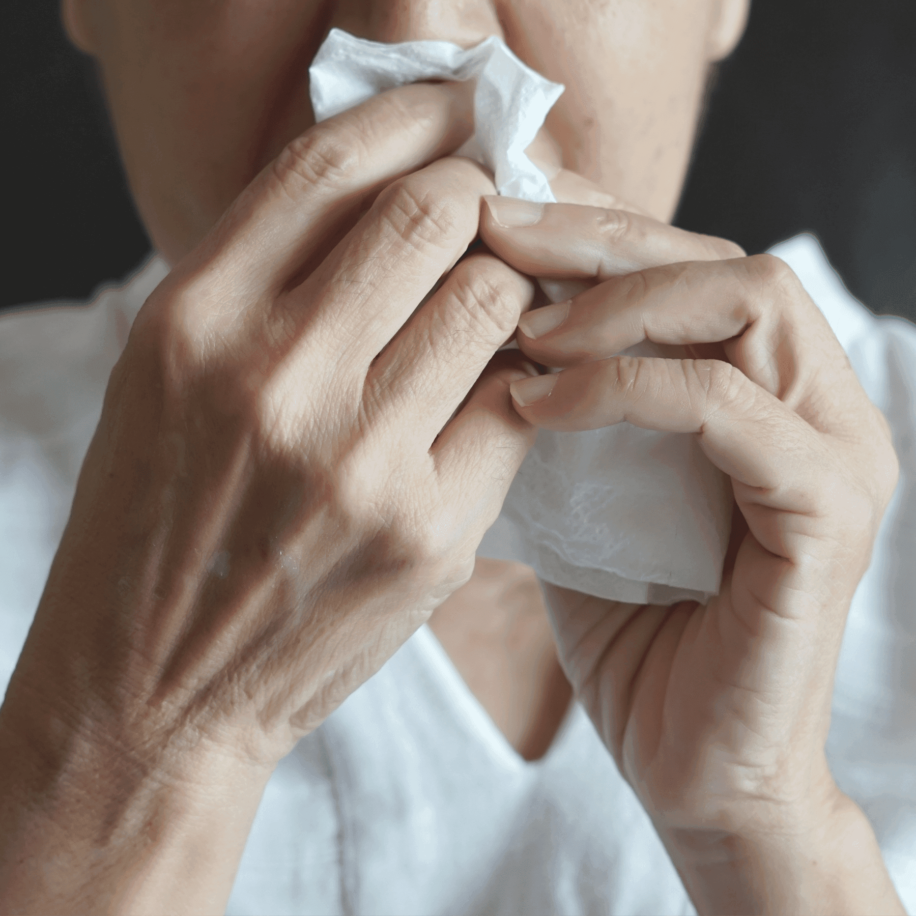 A close-up of a person holding a tissue to their nose with both hands